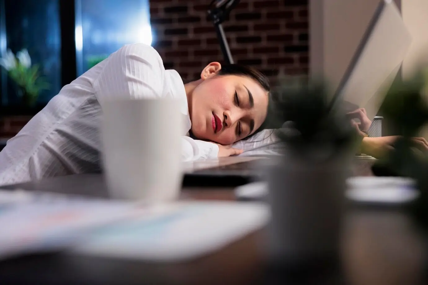 Erschöpfte leitende Managerin mit Burnout-Syndrom ruht wegen Überarbeitung bei der Arbeit. Müde, erschöpfte Geschäftsfrau schläft nach Überstunden auf dem Schreibtisch am Büroarbeitsplatz.